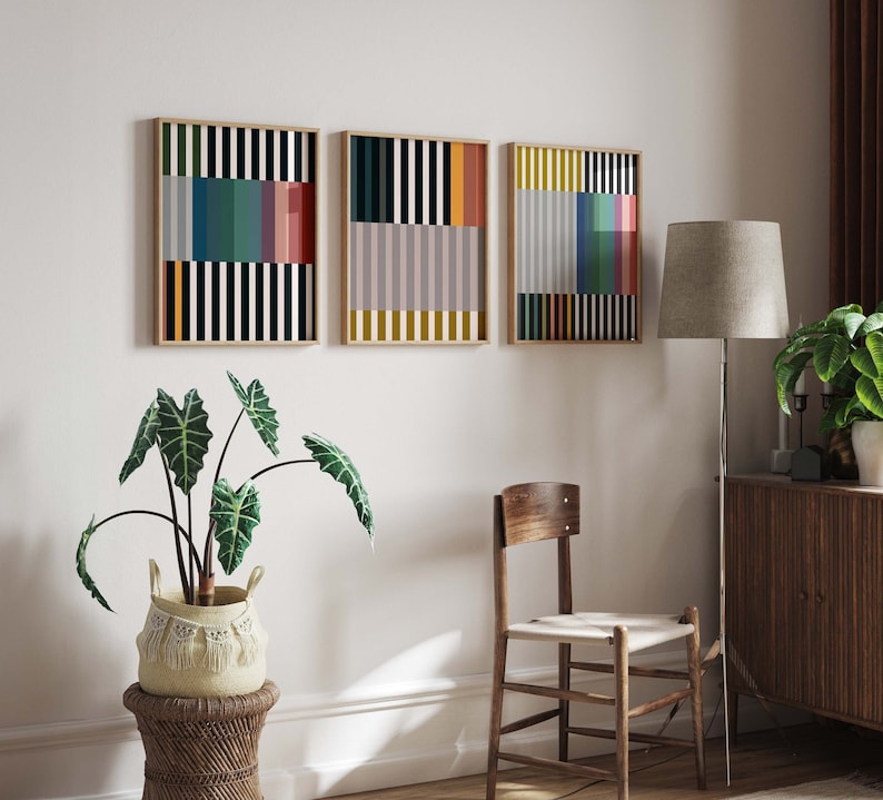 Pode incluir: Tr&ecirc;s impress&otilde;es geom&eacute;tricas abstratas com listras verticais em v&aacute;rias cores, incluindo preto, branco, vermelho, amarelo, azul e verde. As impress&otilde;es s&atilde;o emolduradas em madeira natural e penduradas em uma parede branca.
