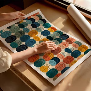 May include: A rectangular art print featuring a repeating pattern of stacked, semi-circular arch shapes in shades of mustard yellow, terracotta orange, teal, dark blue, and soft pink, all set against a light cream-colored background.