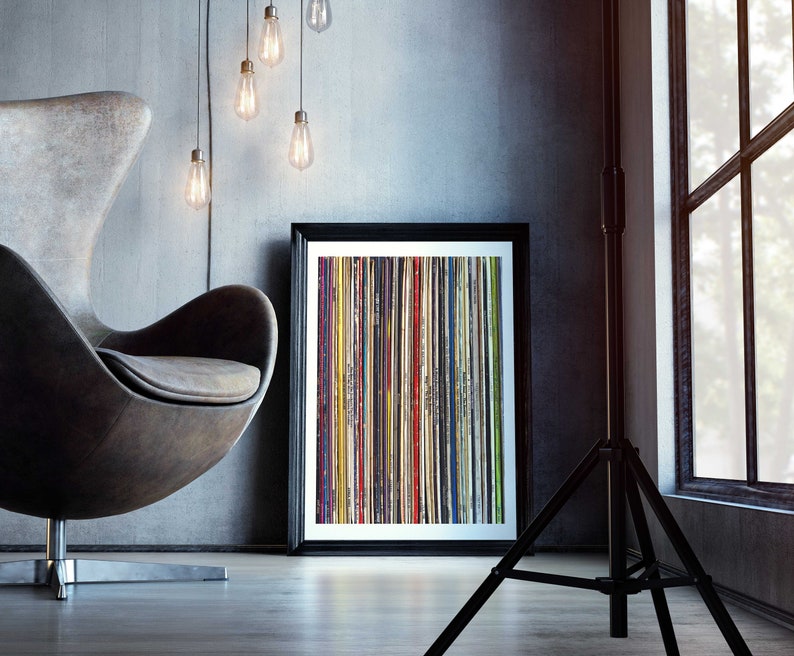 Pu&ograve; includere: Una stampa incorniciata di un design astratto colorato con strisce verticali di vari colori e trame. La stampa &egrave; appesa a una parete grigia in un ambiente di soggiorno moderno.