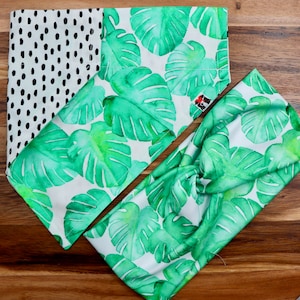 May include: A set of two fabric headbands with a tropical leaf print. The headbands are white with green watercolor leaves. One headband has a black and white polka dot pattern on the back.