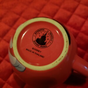 May include: Red ceramic mug with a white and black design. The bottom of the mug features the Disney Parks logo, the words "Authentic Original", and "Made in Thailand".