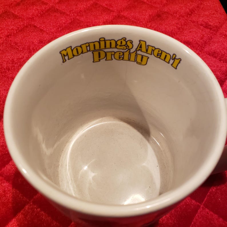 Puede incluir: Taza de caf&eacute; de cer&aacute;mica blanca con el texto "Mornings Aren't Pretty" en letras amarillas. La taza tiene un dise&ntilde;o simple y cl&aacute;sico, perfecto para disfrutar de tu bebida caliente favorita.