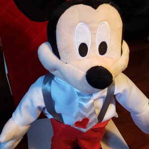 K&ouml;nnte beinhalten: Eine Mickey Mouse Pl&uuml;schpuppe mit wei&szlig;em Hemd, roter Hose und grauer Krawatte mit rotem Herz. Die Puppe hat schwarze Ohren, eine schwarze Nase und wei&szlig;e Gesichtsz&uuml;ge. Ein klassischer Disney-Charakter.