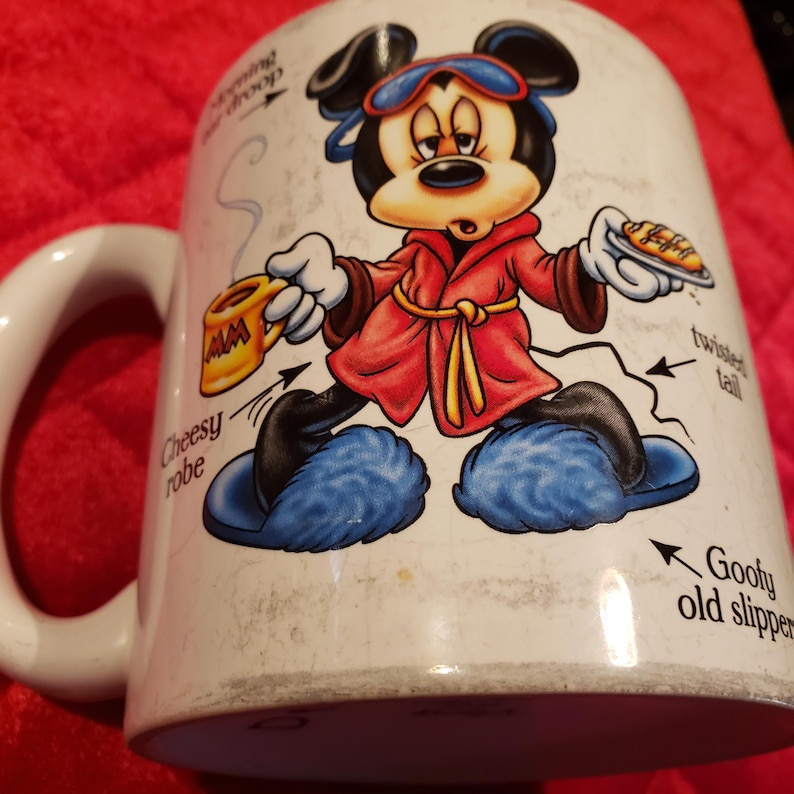 Puede incluir: Taza de cer&aacute;mica blanca con un personaje de dibujos animados de Mickey Mouse con una bata roja y zapatillas azules. La taza tiene las palabras "Cheesy robe", "Morning droop", "Twisted tail" y "Goofy old slipper" impresas.