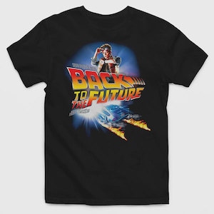 May include: A black short-sleeved t-shirt featuring a graphic print of the Back to the Future movie logo, a character wearing goggles and a vest, and a car leaving trails of fire. The design includes the text Steven Spielberg and Robert Zemeckis.