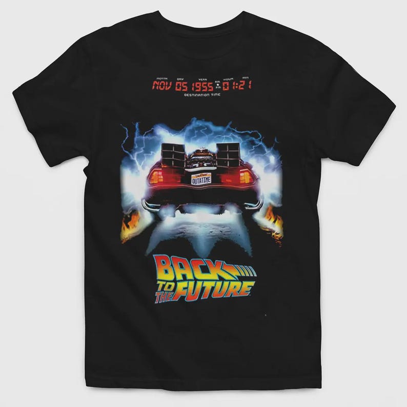 Puede incluir: Una camiseta negra con un gr&aacute;fico de un coche deportivo con una matr&iacute;cula que dice OUTATIME, rodeado de rayos azules y llamas. Sobre el coche, un texto digital rojo dice NOV 05 1955 01:21. Debajo, aparece el texto BACK TO THE FUTURE.