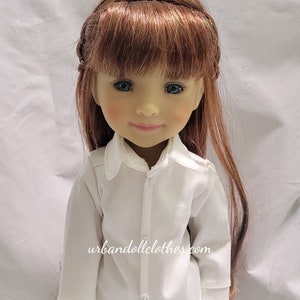Puede incluir: Una camisa blanca de botones con mangas largas y un pantalón vaquero azul. La muñeca lleva el atuendo y tiene el pelo largo y castaño con flequillo.