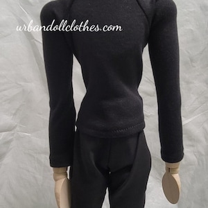 Op de afbeelding: Een zwarte poppenoutfit bestaande uit een top met lange mouwen en een broek. De top heeft een col. De website urbandollclothes.com staat op de achterkant van de top. De outfit wordt getoond op een houten mannequin.