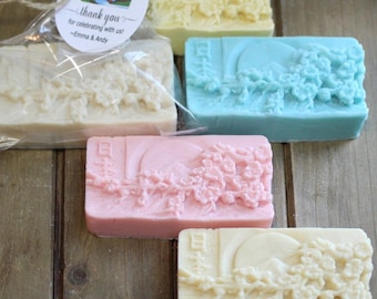 May include: Assortment of rectangular soaps in various pastel colors, each featuring a detailed floral and landscape design. One soap is packaged with a tag that reads "Thank you for celebrating with us! ~Emma & Andy."