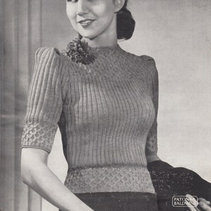 Puede incluir: Una fotografía en blanco y negro de una mujer con un suéter de punto con un patrón de costillas. El suéter tiene un cuello redondo y mangas cortas. La mujer lleva un sombrero y tiene el pelo recogido hacia atrás. La foto es de un libro de patrones de punto vintage.