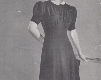May include: A black and white photo of a woman wearing a black dress with a white collar. The dress has puffed sleeves and a fitted bodice. The woman is standing with her hand on a table. The text "Design No.1020 - Price 3º KNITTED IN Sirdar 'KASHA' WOOL 3-PLY" is printed at the top of the image.