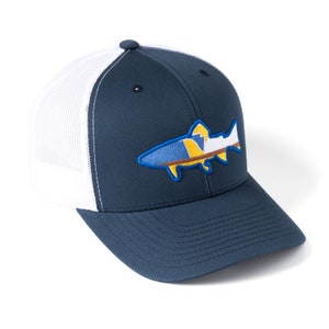 Puede incluir: Gorra de béisbol azul marino con parte trasera de malla blanca. La gorra presenta un diseño de pez bordado en azul, amarillo y blanco. El sombrero tiene una visera curva y un botón en la parte superior.