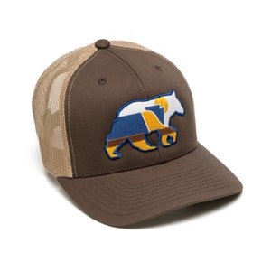 Könnte beinhalten: Eine braune und beige Trucker-Kappe mit einer gestickten Silhouette eines braunen Bären auf der Vorderseite. Der Bär besteht aus verschiedenen farbigen Formen, darunter Blau, Gelb und Weiß.