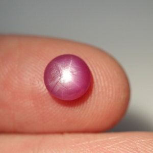 May include: A pink star ruby gemstone with a six-pointed star in the center.
