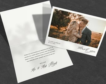 May include: A white wedding thank you card with a photograph of a kissing couple. The card is open, revealing a printed message. The photograph is labeled with names and a date. The words "Thank you" are written in cursive.