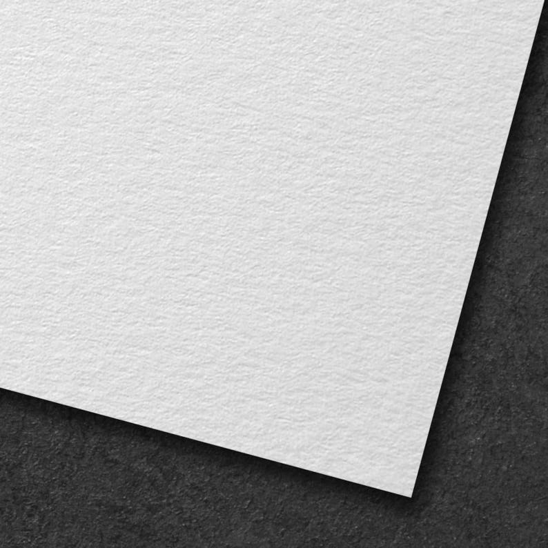 May include: A close-up of a white textured paper corner against a dark gray background. The paper has a slightly rough surface, and the corner is angled, creating a diagonal line across the frame. The paper appears to be thick and high-quality.