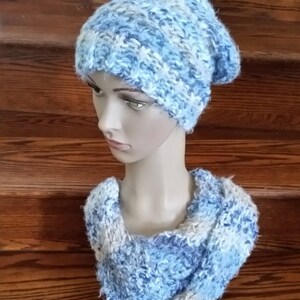 May include: A blue and white knitted hat and matching scarf. The hat is slouchy and the scarf is a cowl style.
