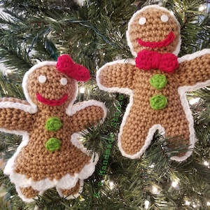 May include: Two crocheted gingerbread people ornaments hanging on a Christmas tree. The gingerbread person on the left is wearing a red bow and the gingerbread person on the right is wearing a red bow tie. Both gingerbread people have green buttons and white icing.