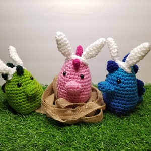 May include: Three crocheted Easter egg-shaped plushies with bunny ears. The plushies are green, pink, and blue.