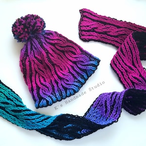 May include: A crocheted hat and scarf set in a gradient of pink, purple, blue and black with a black pom pom on the hat. The scarf is shown in two different positions.