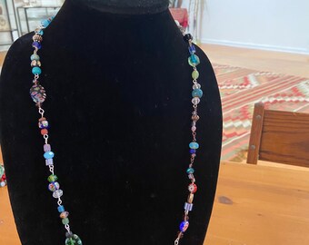 May include: A colorful glass bead necklace with a variety of shapes and sizes. The necklace is displayed on a black velvet bust form.