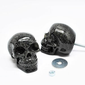 May include: Two black skull-shaped cabinet knobs with a glittery finish. The knobs have a screw and a washer.