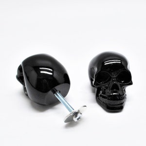 May include: Two black skull-shaped cabinet knobs with a silver screw and washer. The knobs are glossy and have a detailed skull design.