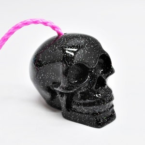 May include: Black skull shaped ornament with glitter finish and a pink string attached to the top.