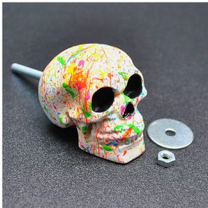 May include: White skull-shaped cabinet knob with colorful paint splatters. The knob has a silver screw and washer.