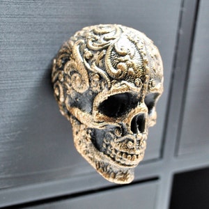 May include: A black and gold skull-shaped cabinet knob with intricate floral designs.