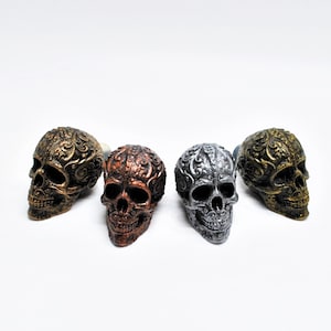 May include: Four decorative skull ornaments with intricate designs. The skulls are in gold, silver, and copper finishes.