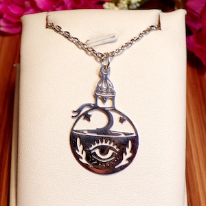 May include: A silver necklace with a pendant shaped like a bottle with a crescent moon, stars, and an eye inside. The pendant is on a white display stand.