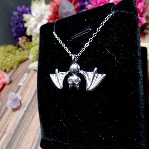 Pu&ograve; includere: Una collana di pipistrello d'argento con un piccolo ciondolo di pipistrello dettagliato. Il pipistrello ha due piccoli strass trasparenti per gli occhi. La collana &egrave; esposta su uno sfondo di velluto nero.