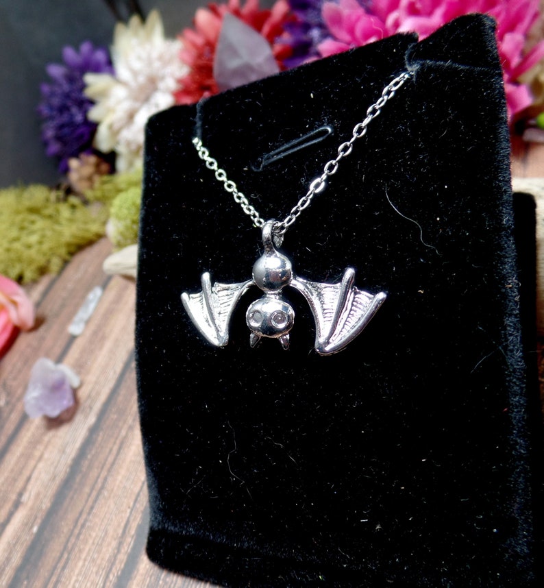 Pu&ograve; includere: Una collana di pipistrello d'argento con un piccolo ciondolo di pipistrello dettagliato. Il pipistrello ha due piccoli strass trasparenti per gli occhi. La collana &egrave; esposta su uno sfondo di velluto nero.