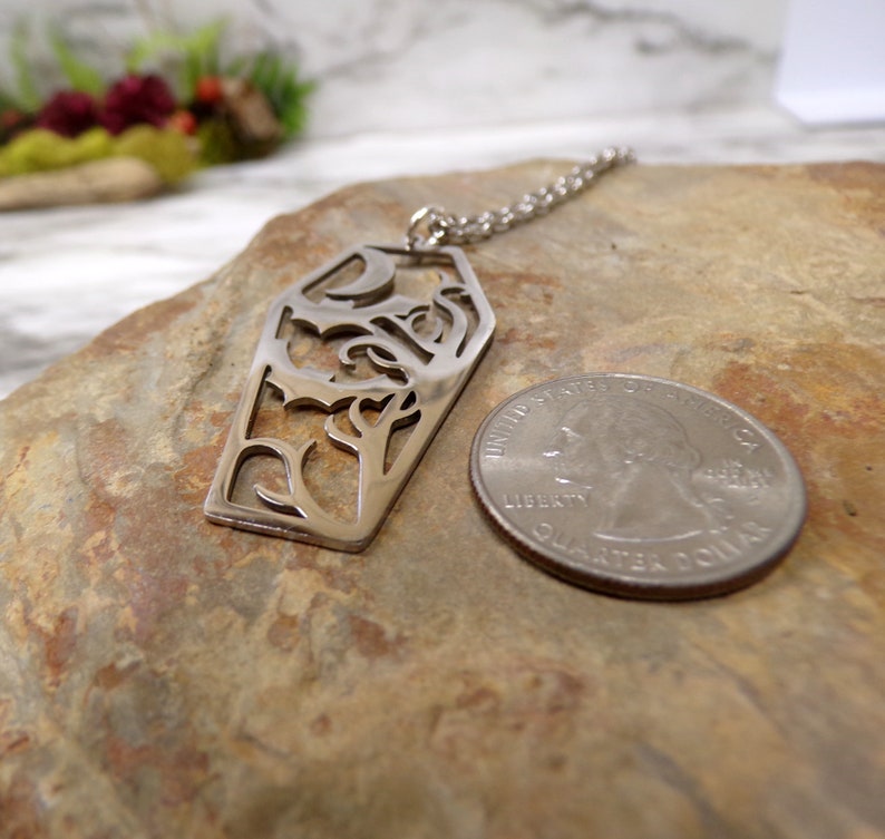 Pu&ograve; includere: Collana con ciondolo in argento con un designo a taglio dettagliato di una bara con una luna crescente e viti. Il ciondolo &egrave; mostrato accanto a una moneta da 1 euro per il confronto delle dimensioni.