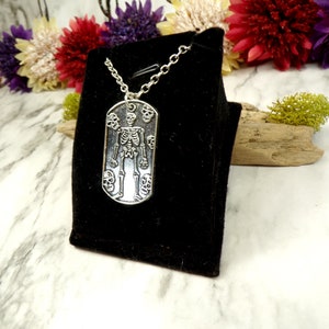 May include: A silver necklace with a skeleton pendant surrounded by skulls. The pendant is on a black velvet background.