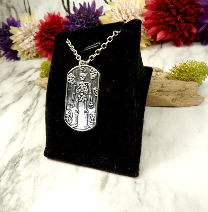 May include: A silver necklace with a skeleton pendant surrounded by skulls. The pendant is on a black velvet background.