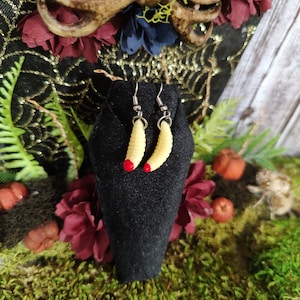 May include: A pair of earrings featuring a yellow and red worm design. The earrings are displayed on a black velvet stand.