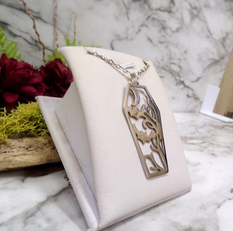 Pu&ograve; includere: Una collana d'argento con un ciondolo a forma di bara con un design dettagliato e intricato. Il ciondolo &egrave; tagliato, rivelando il design.