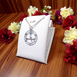 May include: A silver necklace with a circular pendant featuring a pentagram symbol. The pendant is on a white display stand.