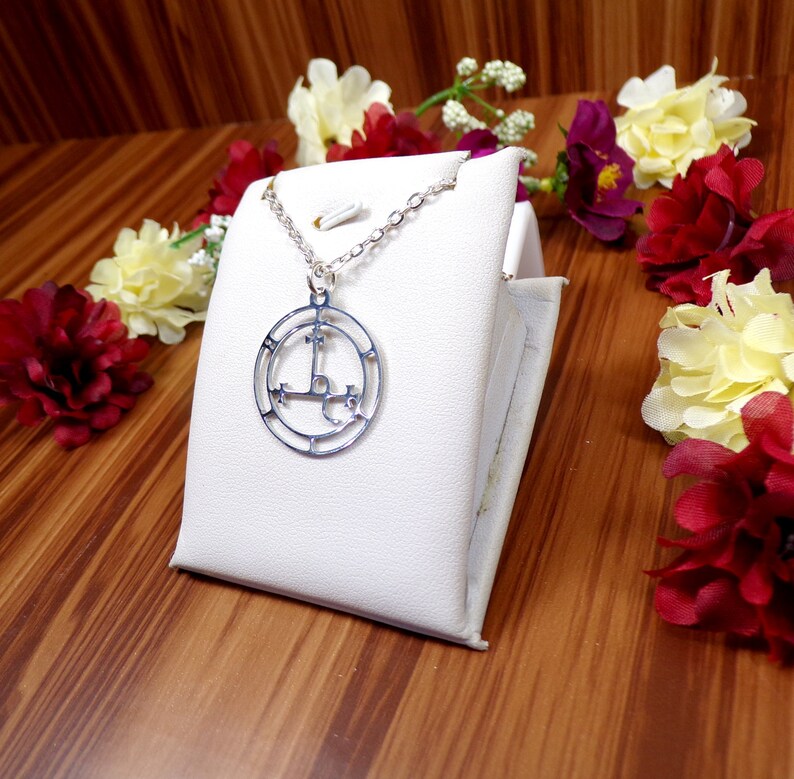 May include: A silver necklace with a circular pendant featuring a pentagram symbol. The pendant is on a white display stand.