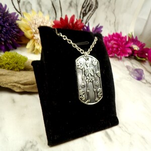 May include: A silver skeleton pendant necklace with a skull design. The pendant is on a black velvet background.