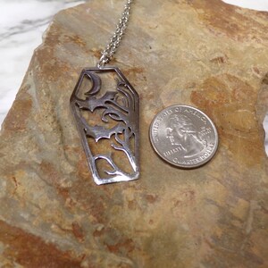 Pu&ograve; includere: Una collana d'argento con un ciondolo a forma di bara con una luna crescente e intricati motivi floreali. Il ciondolo &egrave; circa delle dimensioni di una moneta da 25 centesimi di dollaro americano.