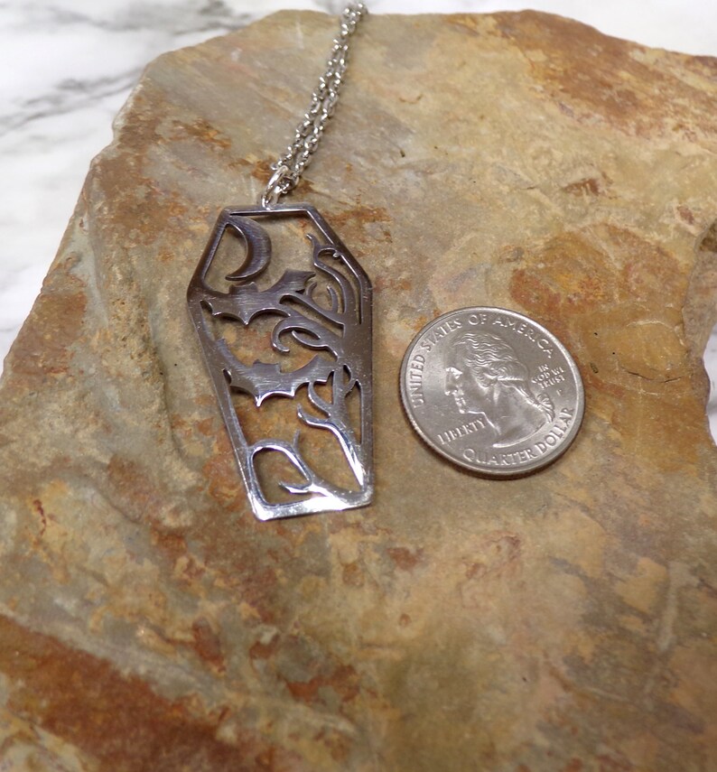 Pu&ograve; includere: Una collana d'argento con un ciondolo a forma di bara con una luna crescente e intricati motivi floreali. Il ciondolo &egrave; circa delle dimensioni di una moneta da 25 centesimi di dollaro americano.