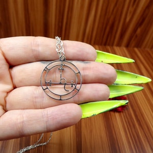 May include: A silver necklace with a circular pendant featuring a sigil with a cross and other symbols. The pendant is on a silver chain.