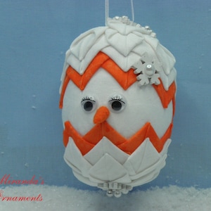 May include: White and orange felt Christmas ornament shaped like an egg with a snowflake and googly eyes.