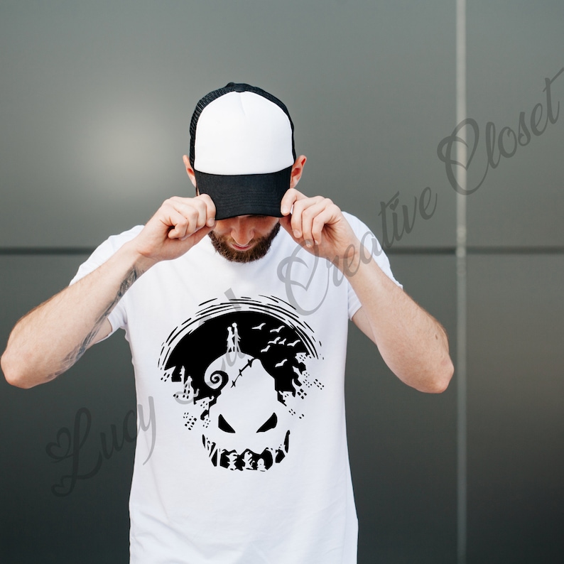 May include: A white t-shirt with a black silhouette of Jack Skellington's face from the movie "The Nightmare Before Christmas". The silhouette is surrounded by trees and birds. The person wearing the shirt is holding a black and white baseball cap.
