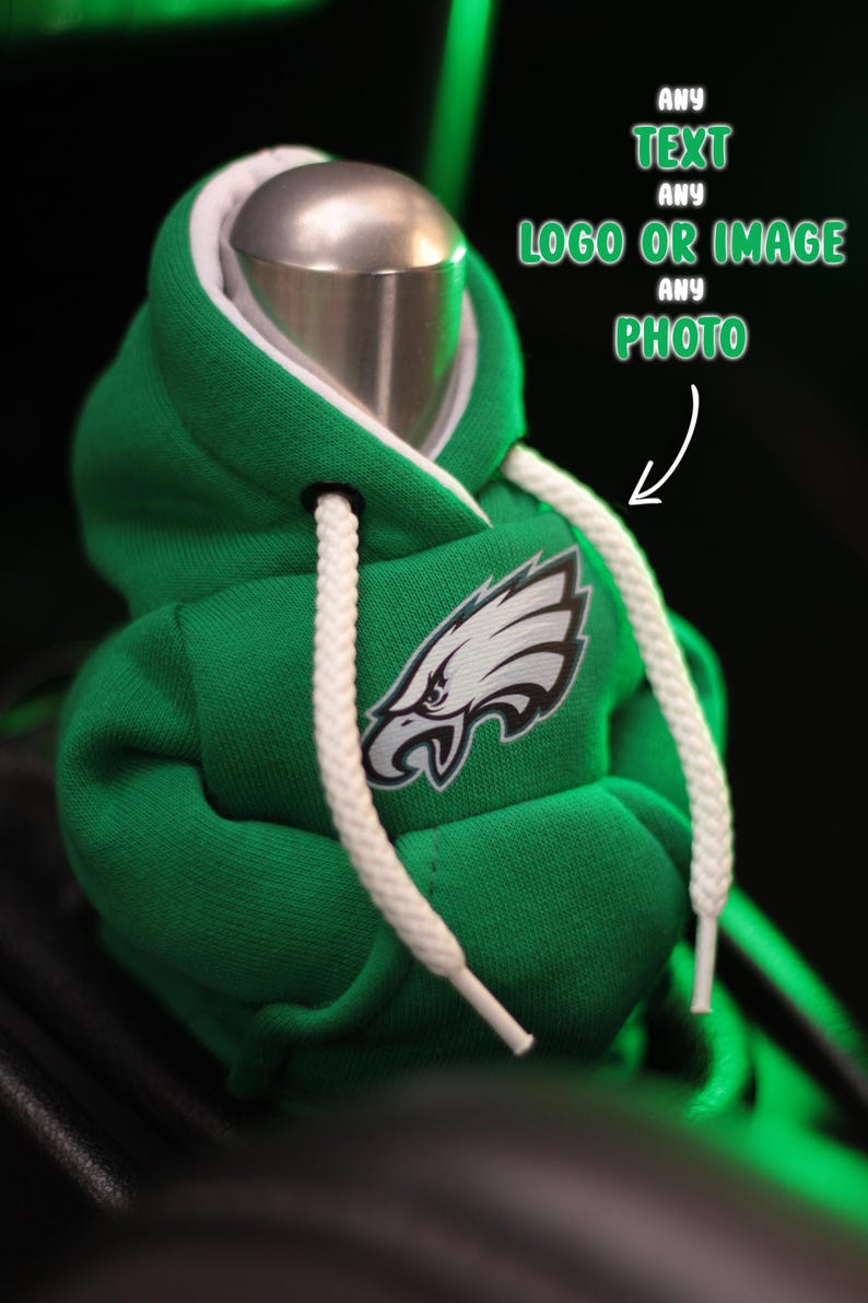 May include: Green hooded sweatshirt with white drawstrings and a Philadelphia Eagles logo on the front.  The sweatshirt is on a car gear shift.