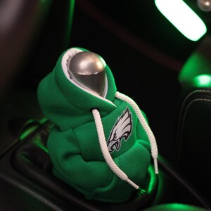 May include: Green hooded sweatshirt gear shifter cover with a white drawstring and an embroidered Philadelphia Eagles logo.