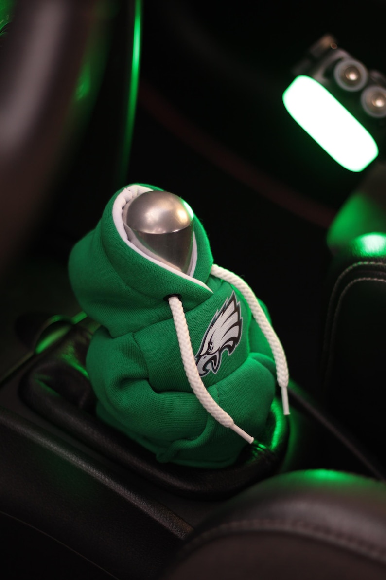 May include: Green hooded sweatshirt gear shifter cover with a white drawstring and an embroidered Philadelphia Eagles logo.